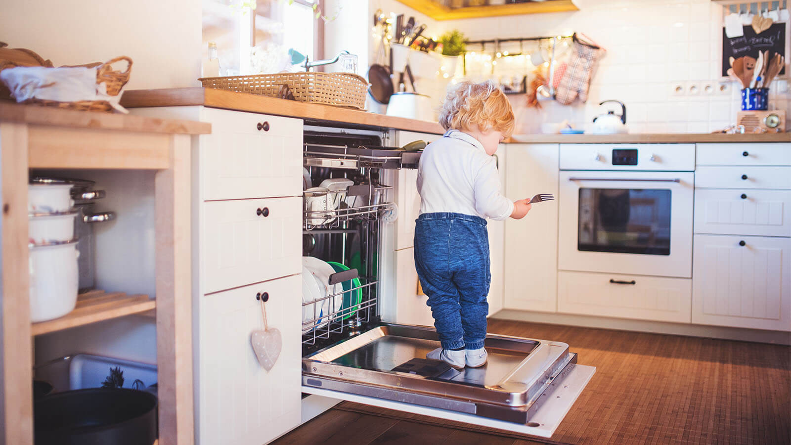 criança em posição de risco na cozinha, em cima da porta da máquina de lavar loiça