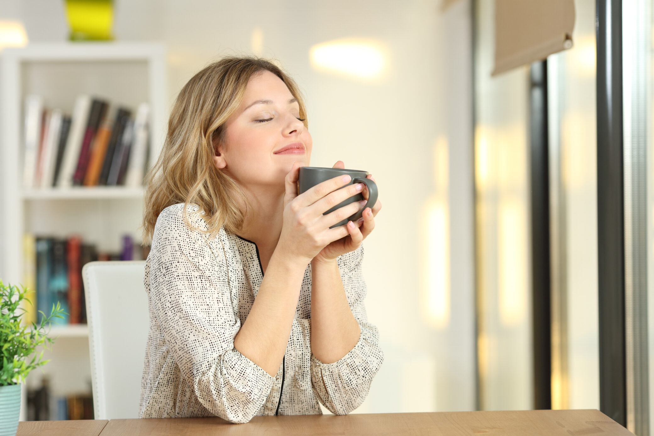Saúde mental - mulher de olhos fechados e a sorrir enquanto segura caneca de café nas mãos