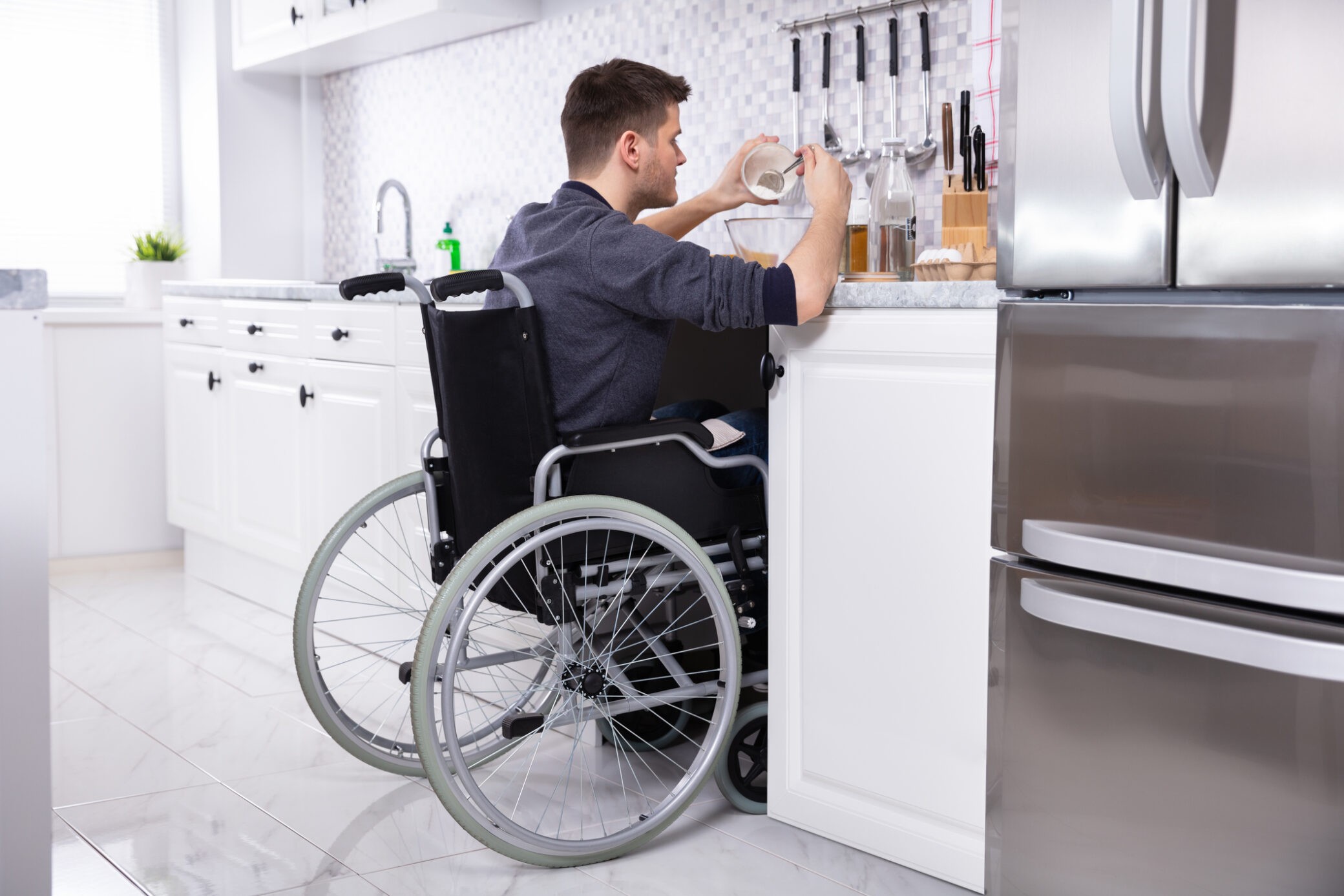 Homem em cadeira de rodas a preparar refeição numa cozinha adaptada a pessoas com incapacidade