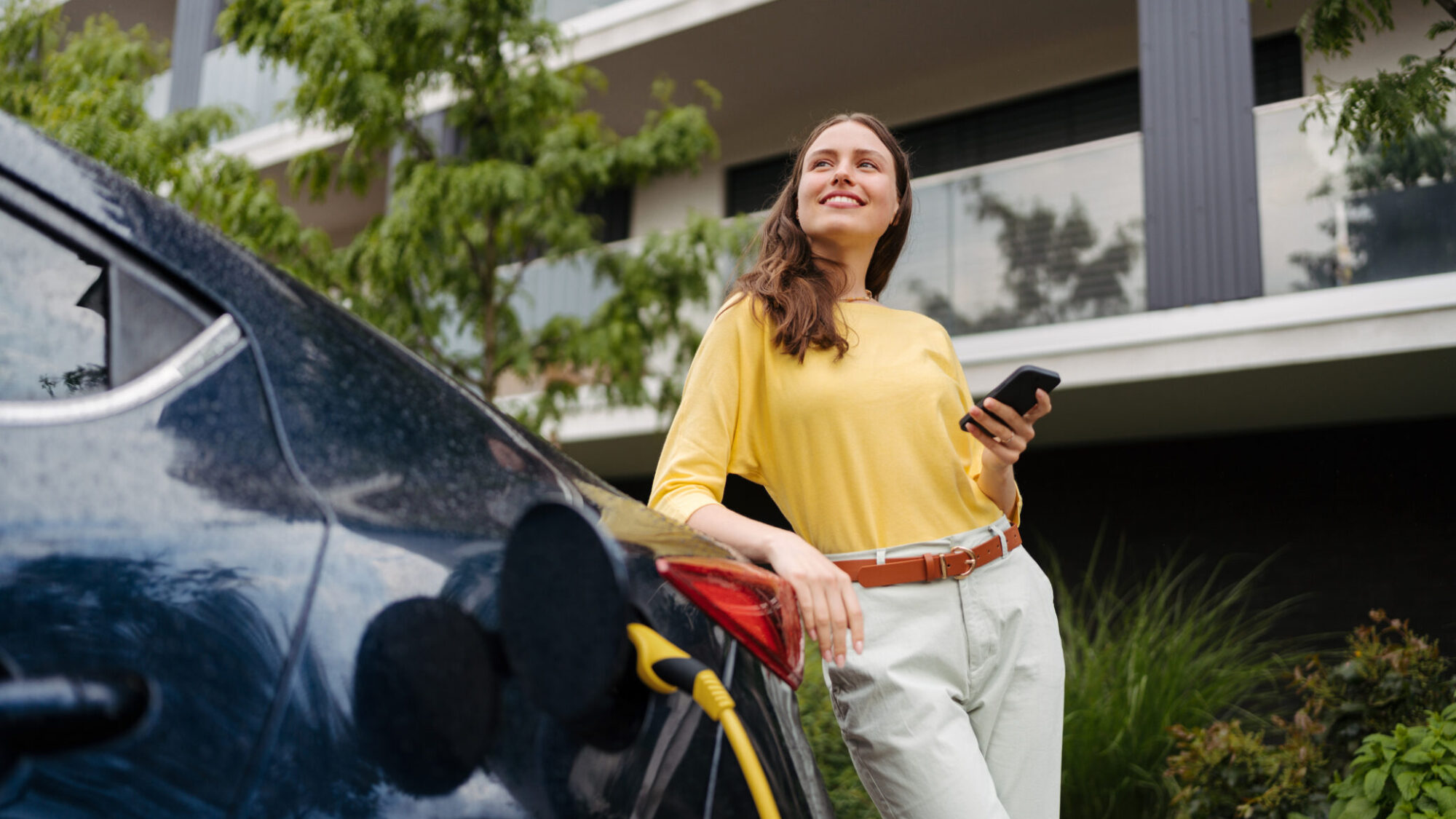 Mulher jovem junto a um carro elétrico que está a ser carregado