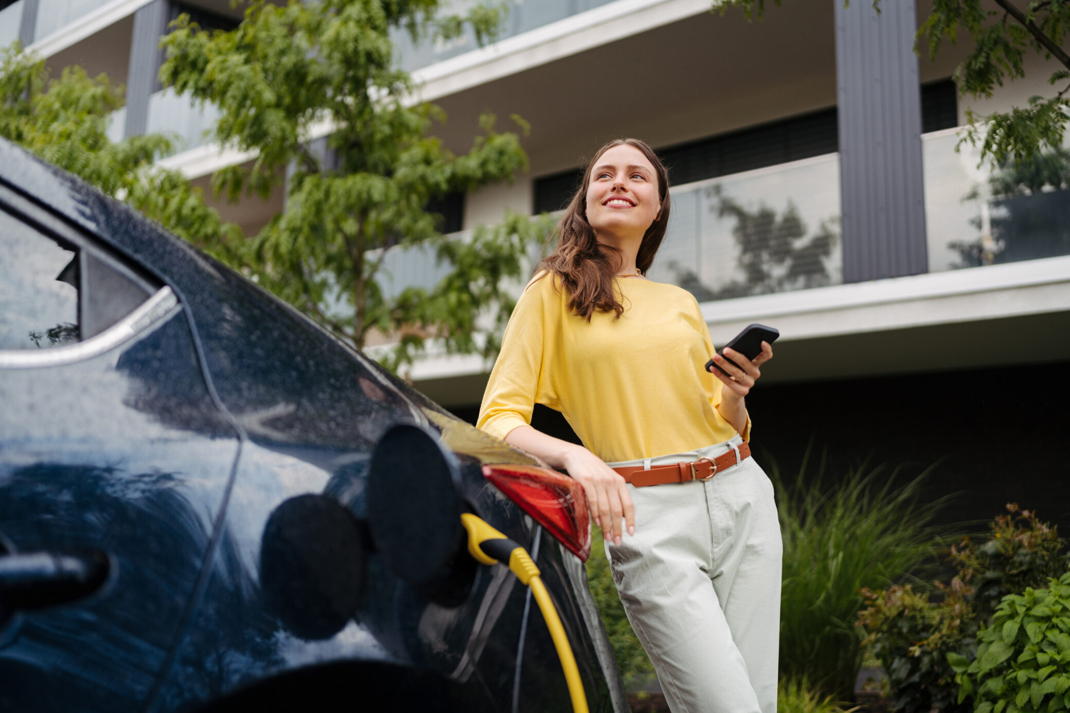 Mulher jovem junto a um carro elétrico que está a ser carregado