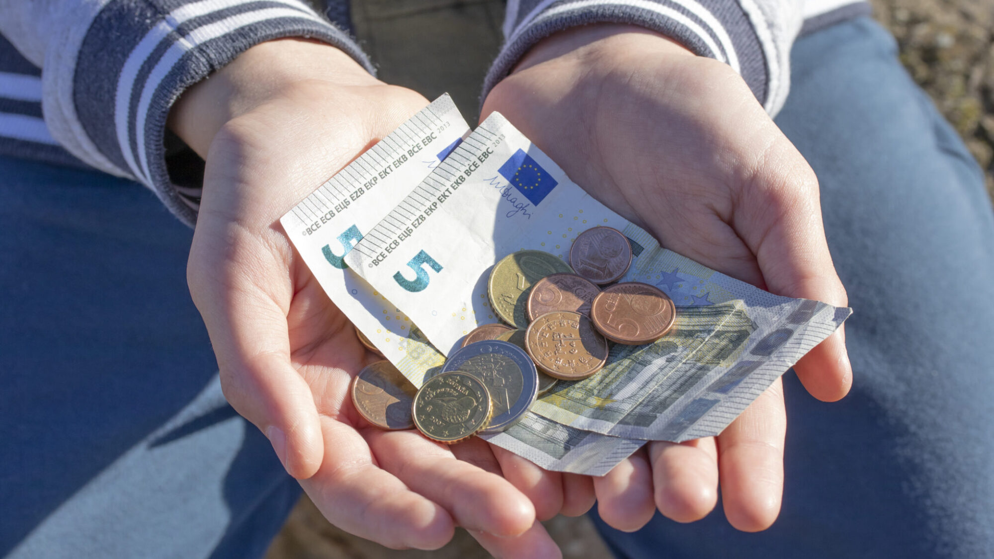 Duas mãos a segurarem várias notas e moedas de Euro, simbolizando o mínimo de existência