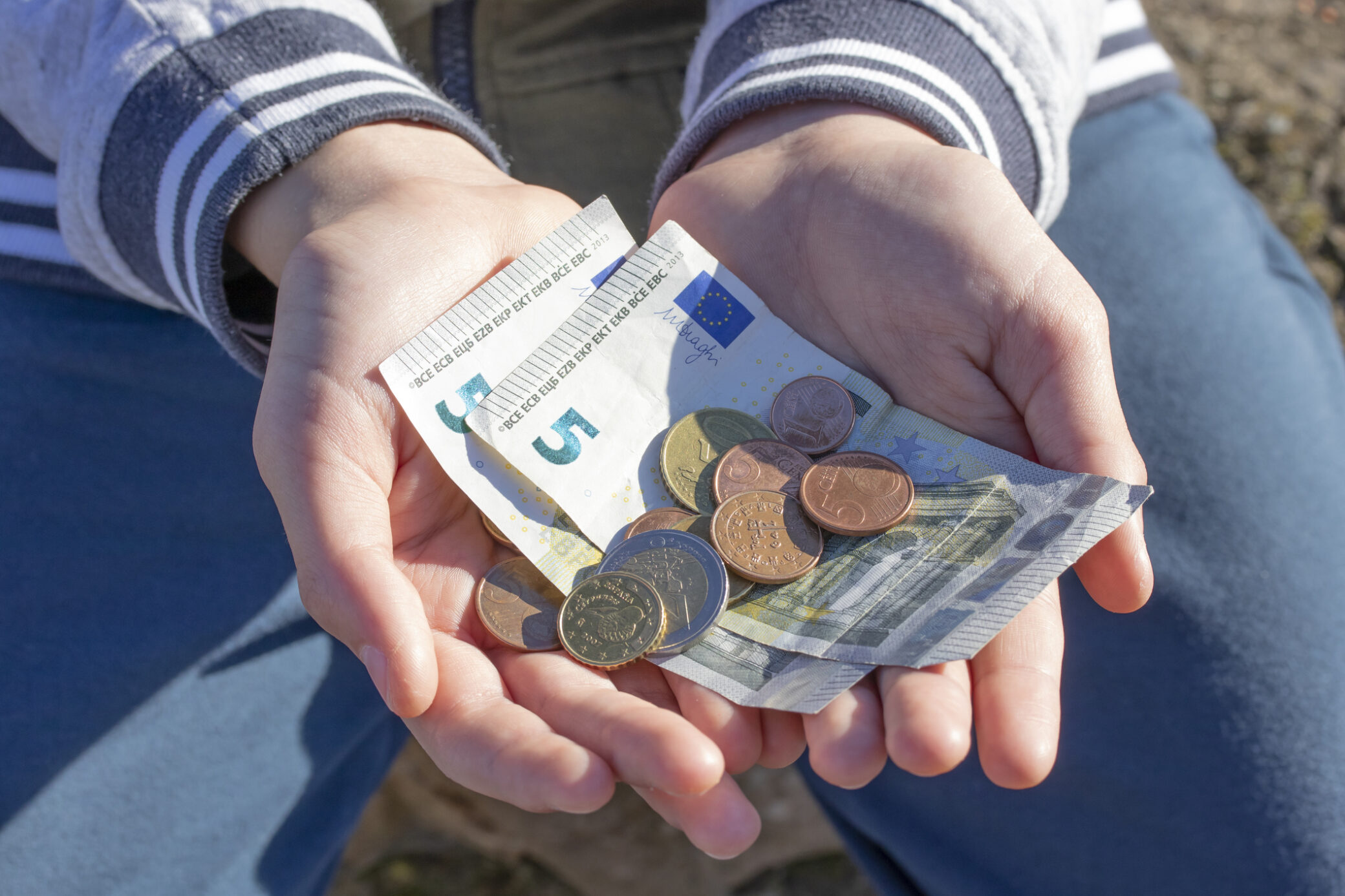 Duas mãos a segurarem várias notas e moedas de Euro, simbolizando o mínimo de existência