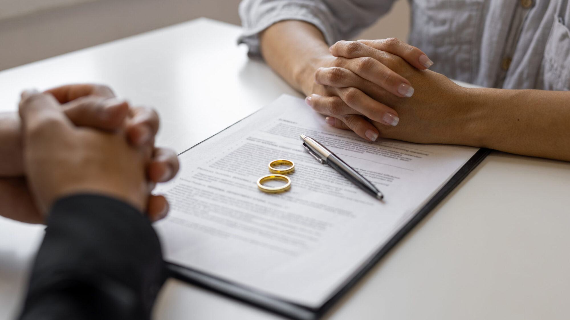 Duas pessoas a assinarem papéis de casamento com duas alianças em cima dos mesmos.