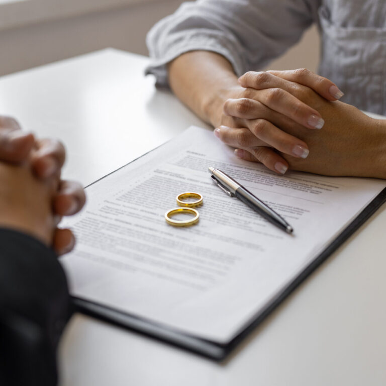 Duas pessoas a assinarem papéis de casamento com duas alianças em cima dos mesmos.